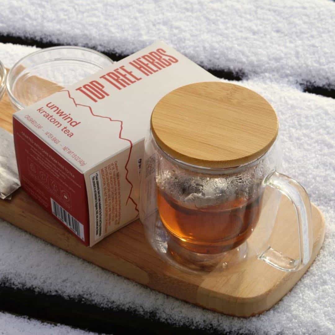 Double-wall glass mug with tea and tea box, staying warm in the snow