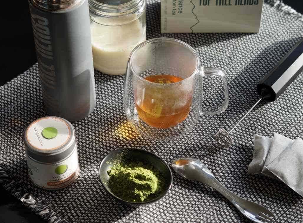 Kratom matcha latte ingredients and equipment: milk, tea, vanilla matcha powder, plus a thermos and a frother. 